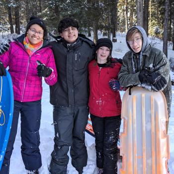 A group of teens posing with sleds at their winter retreat.